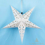 Étoile en papier blanche à motifs étoiles et lunes ajourés, suspendue sur fond bleu texturé