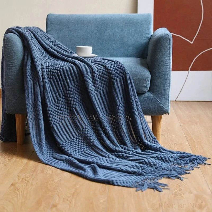 Plaid de Noël bleu marine drapé sur un fauteuil bleu, tasse de café posée sur l'accoudoir