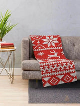 Plaid tricoté rouge à motifs rennes et flocons blancs, drapé sur un canapé gris dans un salon