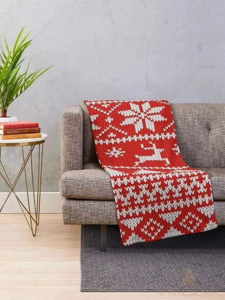 Plaid tricoté rouge à motifs rennes et flocons blancs, drapé sur un canapé gris dans un salon