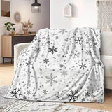 Plaid de Noël blanc à motif de flocons noirs et gris, sans personnage, posé sur un fauteuil