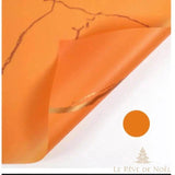 Papier cadeau effet marbre orange, coin replié laissant voir une veine dorée sur l'envers