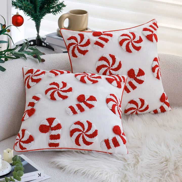 Deux coussins blancs à motifs sucre d'orge et bonbons brodés en relief, posés sur un canapé près d'un sapin
