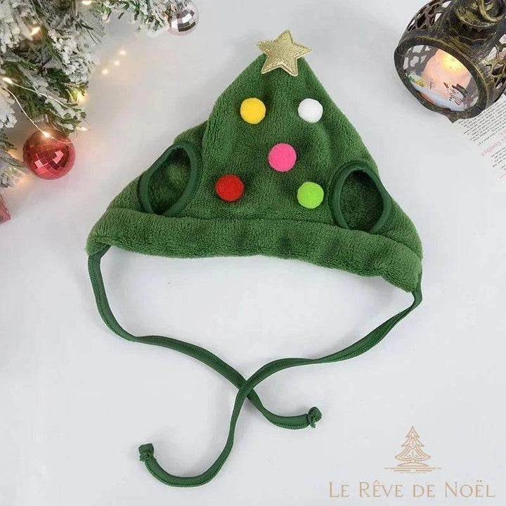 Bonnet de Noël vert en forme de sapin avec pompons colorés, posé à plat près d'une lanterne allumée