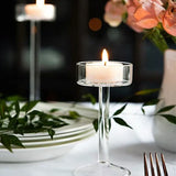 Bougeoir en verre avec bougie allumée sur une table dressée, roses et assiettes en fond