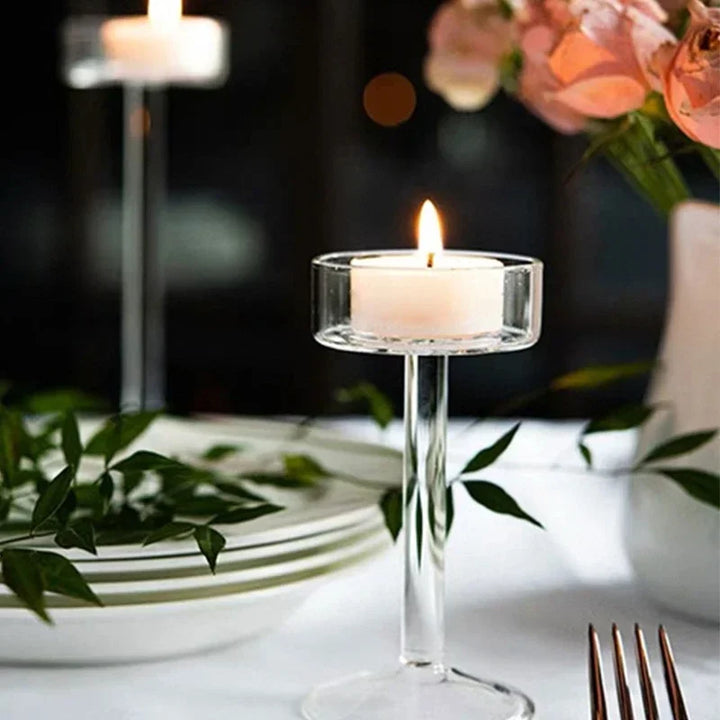 Bougeoir en verre avec bougie allumée sur une table dressée, roses et assiettes en fond