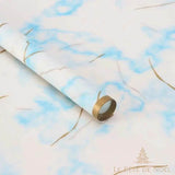 Rouleau de papier cadeau effet marbre blanc et bleu ciel, entouré de rubans dorés bouclés
