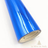 Papier cadeau métallisé bleu brillant, enroulé en rouleau montrant l'envers blanc du papier
