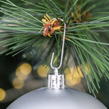 Attache en métal d'une boule de Noël argentée accrochée à une branche de sapin