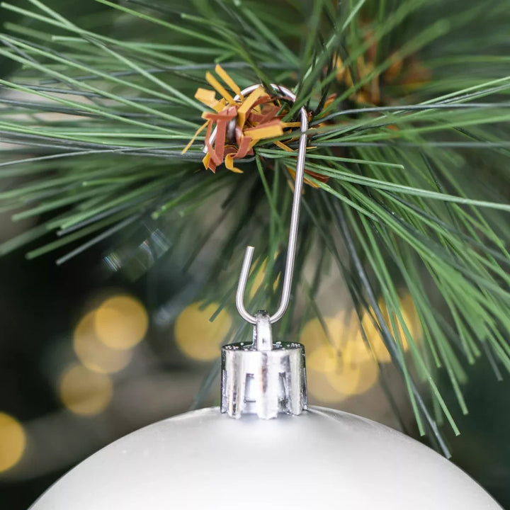 Attache en métal d'une boule de Noël blanche accrochée à une branche de sapin