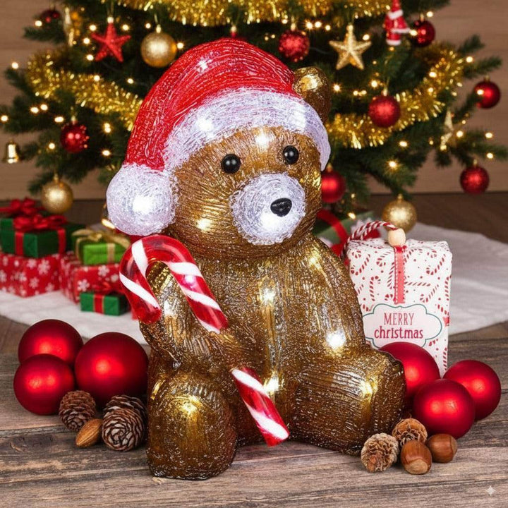 Ours de Noël lumineux brun doré, bonnet de Père Noël et canne en sucre d'orge, devant un sapin