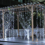 Rideau lumineux LED blanc froid suspendu à une pergola, éclairant une terrasse en bois la nuit
