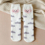 Paire de chaussettes pelucheuses blanches à motifs de nuages gris, posées sur un plaid beige