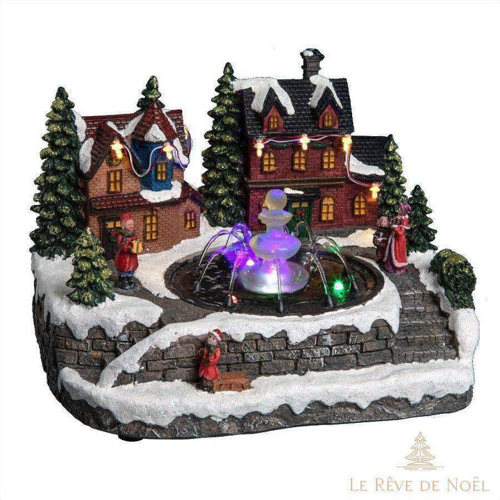 Village de Noël miniature avec maisons illuminées, sapins enneigés et fontaine à LED colorée