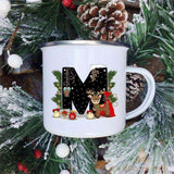 Mug émaillé blanc à lettre M noire décorée d'un faon en cape rouge, sur fond de sapin étoilé