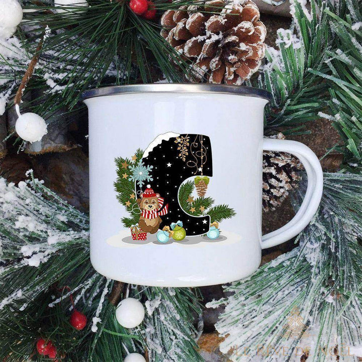 Mug émaillé blanc à lettre C noire ornée d'un ourson au bonnet et écharpe rayée, fond de sapin enneigé
