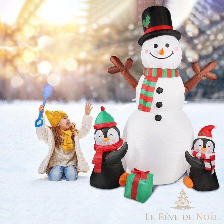 Bonhomme de neige gonflable dans un jardin enneigé le jour, une fillette joue à côté avec une pelle