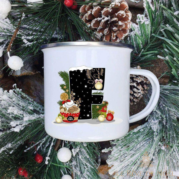 Mug lettre F posé parmi des branches de sapin enneigées, motif cupcake et guirlande dorée