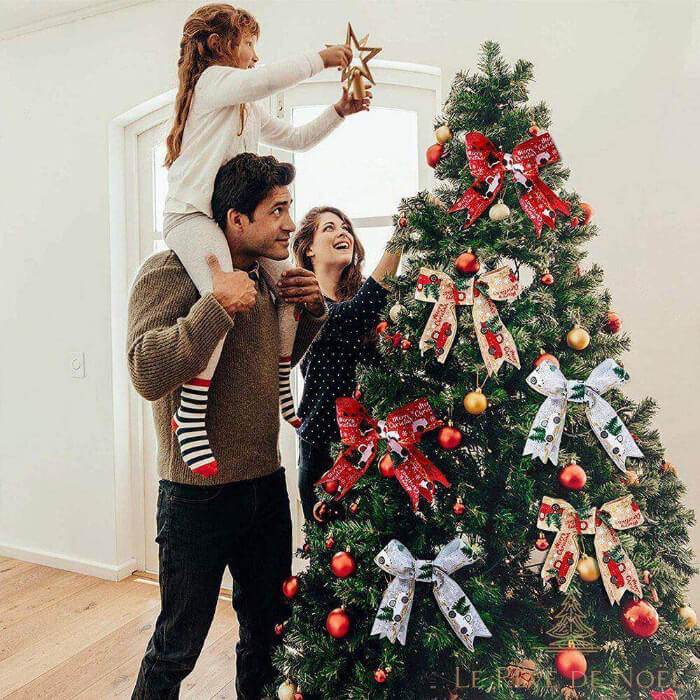Famille nouant des nœuds en ruban à motif camion sur les branches d'un sapin décoré