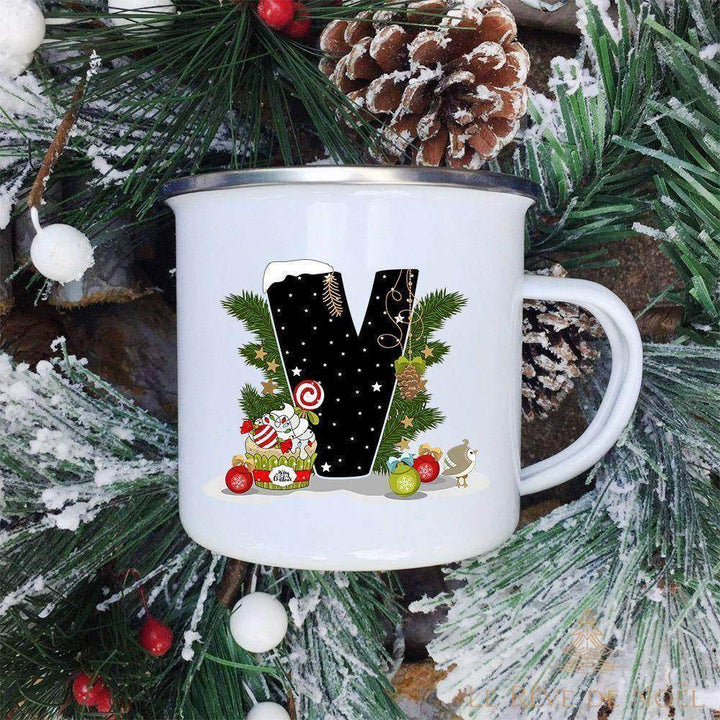 Mug émaillé blanc à lettre V noire décorée d'un cupcake glacé et d'un oiseau, sur fond de sapin