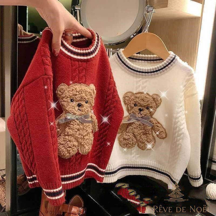 Deux pulls de Noël enfant à ourson brodé, un rouge tenu à la main et un blanc sur cintre