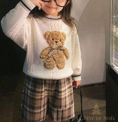 Fillette portant un pull de Noël blanc à ourson brodé, avec un short à carreaux