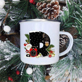 Mug émaillé blanc à lettre R noire décorée d'un Père Noël et d'un réveil rouge, sur fond de sapin