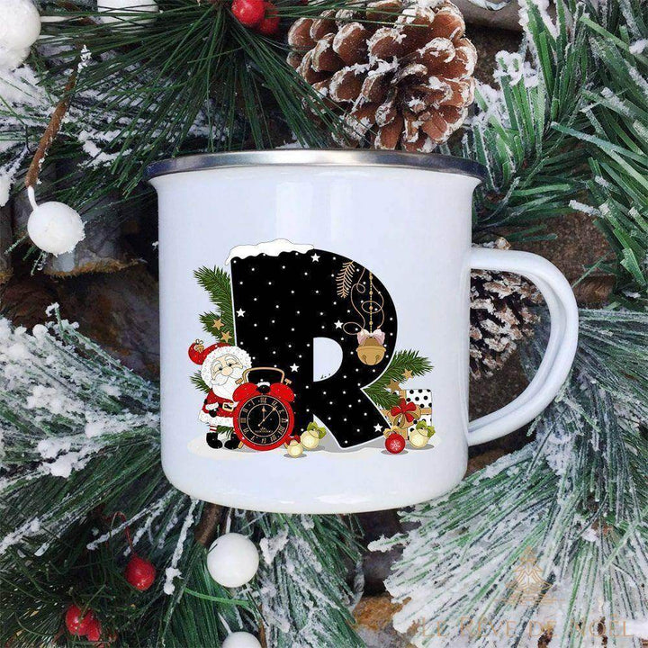 Mug émaillé blanc à lettre R noire décorée d'un Père Noël et d'un réveil rouge, sur fond de sapin