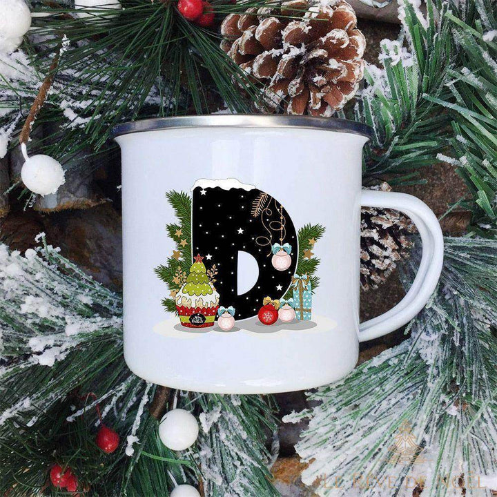 Mug émaillé blanc à lettre D noire ornée d'un cupcake et d'un sapin miniature, sur branches de sapin givrées