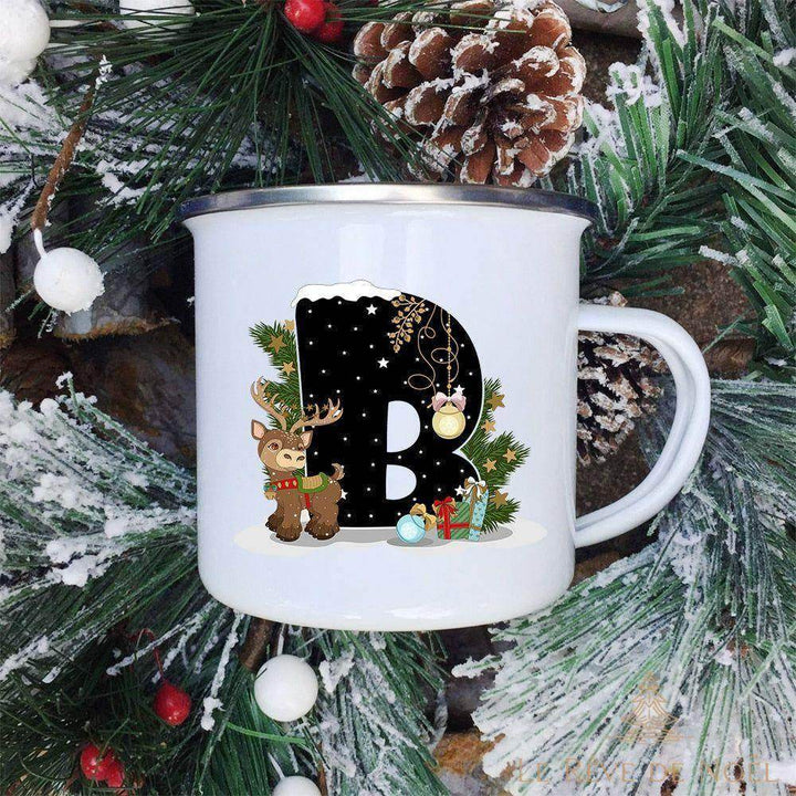 Mug émaillé blanc à lettre B noire ornée d'un faon aux bois et d'un cadeau bleu, fond de sapin enneigé