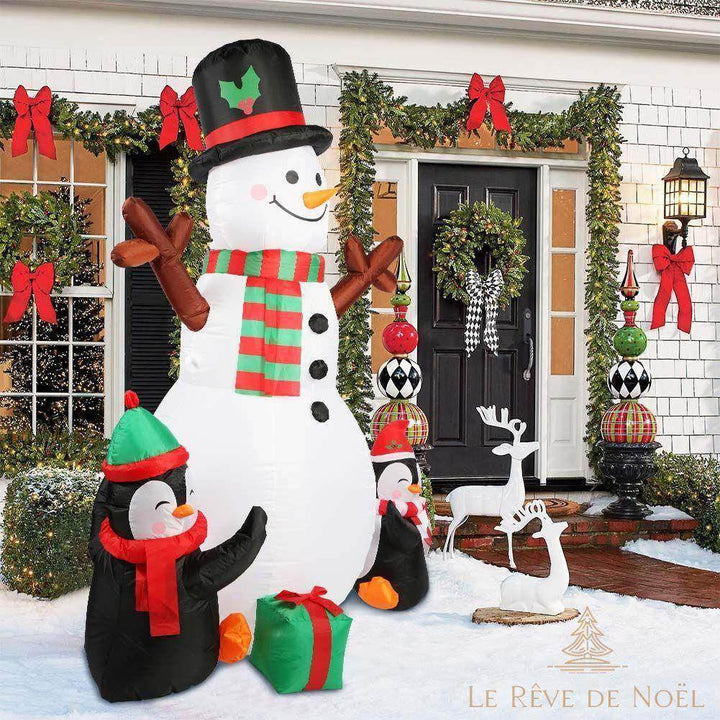 Bonhomme de neige gonflable géant et deux pingouins installés devant une maison décorée la nuit