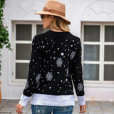 Pull de Noël femme noir à flocons blancs, porté de dos par une femme au chapeau, en extérieur