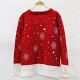 Pull de Noël femme rouge à flocons blancs, vu de dos, suspendu sur un cintre en bois