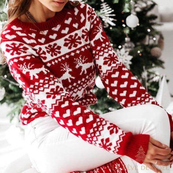 Pull tricot jacquard rouge et blanc à cœurs, rennes et flocons, femme assise devant un sapin