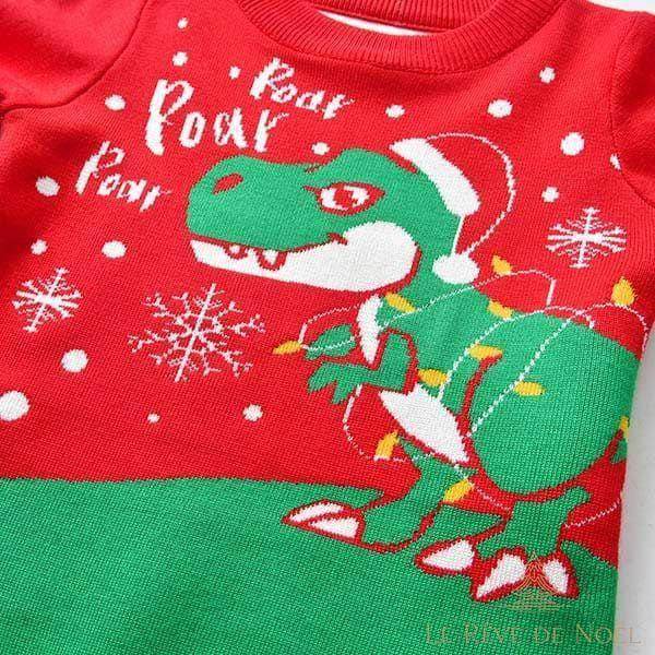 Gros plan sur un pull de Noël enfant rouge et vert, dinosaure en bonnet de Père Noël et guirlande