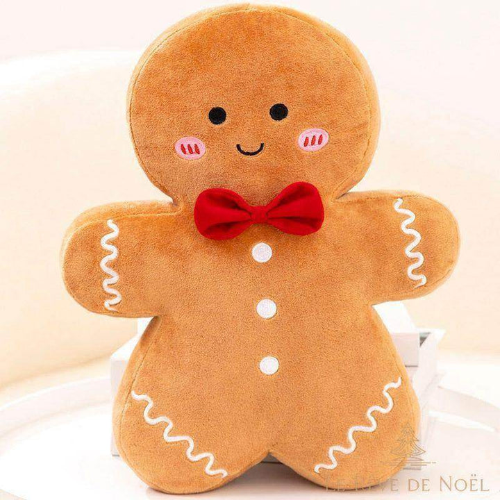 Peluche bonhomme en pain d'épices assise sur des coussins, nœud papillon rouge, glaçage blanc brodé