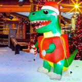 Dinosaure gonflable vert à bonnet rouge et paquet cadeau, installé dehors la nuit dans la neige
