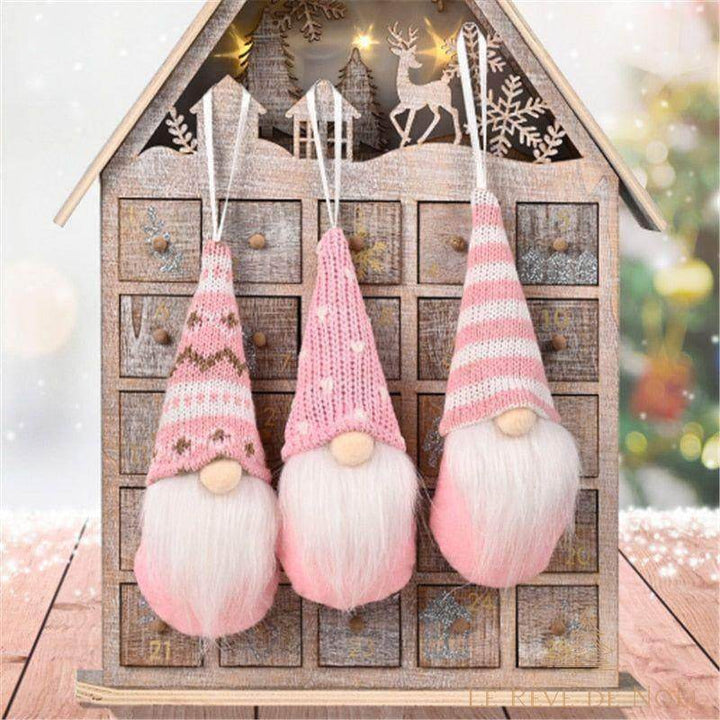 Trois lutins de Noël roses à bonnet tricoté, suspendus par un ruban devant un calendrier en bois