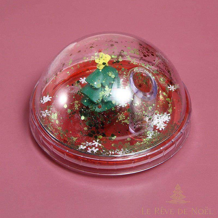 Gros plan sur le dôme pailleté du gobelet, sapin miniature vert et confettis dorés en suspension