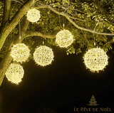 Plusieurs boules lumineuses en osier tressé suspendues à un arbre, lumière blanc chaud la nuit