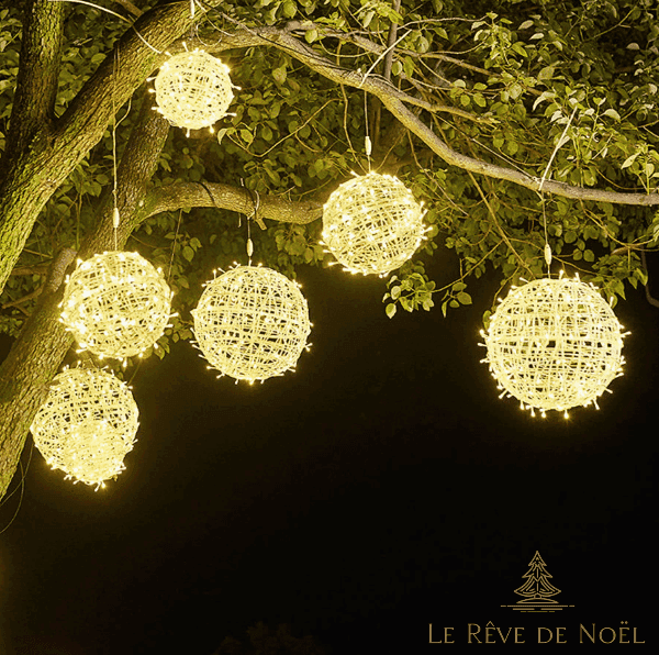 Plusieurs boules lumineuses en osier tressé suspendues à un arbre, lumière blanc chaud la nuit
