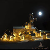 Guirlande de petites maisons lumineuses la nuit, pleine lune et silhouette de renne flous en fond