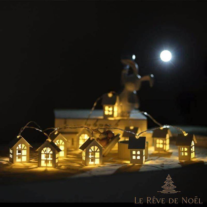 Guirlande de petites maisons lumineuses la nuit, pleine lune et silhouette de renne flous en fond