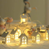 Guirlande de petites maisons lumineuses alignées sur une table, bonhomme de neige flou en arrière-plan
