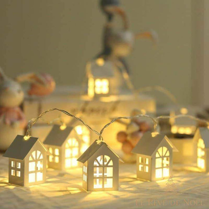 Guirlande de petites maisons lumineuses alignées sur une table, bonhomme de neige flou en arrière-plan