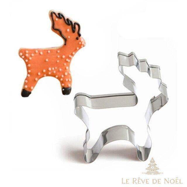 Emporte-pièce métallique en forme de renne, posé à côté d'un biscuit décoré orange et blanc