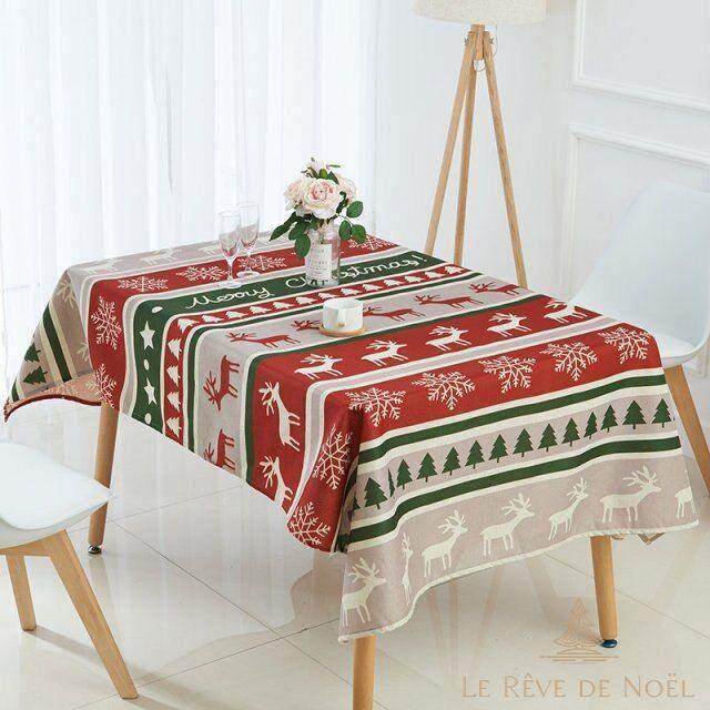 Nappe à rayures rouges, vertes et beiges avec rennes et sapins, dressée sur une table avec fleurs et bougie