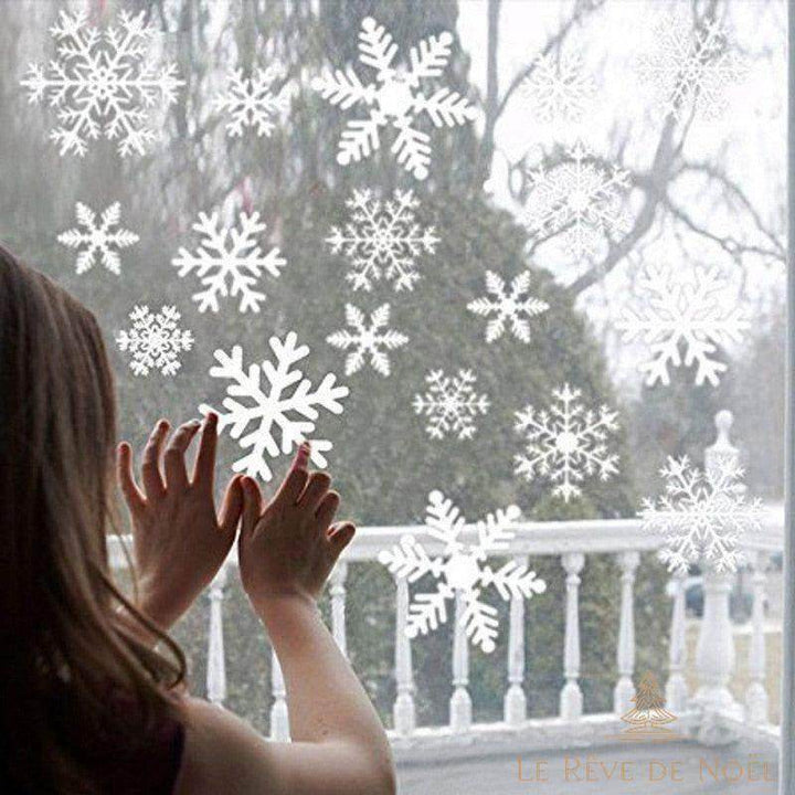 Stickers flocons de neige blancs collés sur une vitre, une fillette y pose les mains