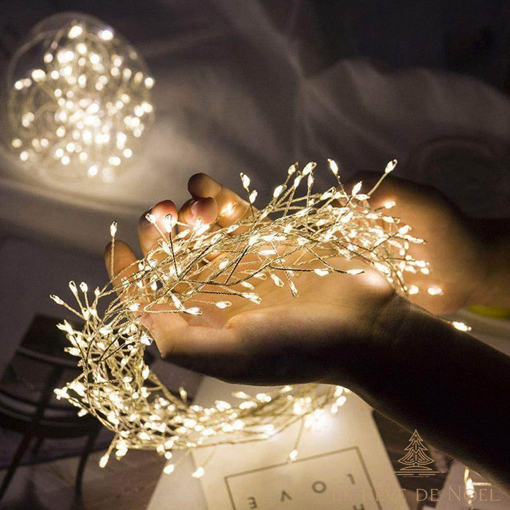 Mains tenant un amas de guirlande lumineuse blanc chaud, dans une pièce sombre
