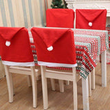 Housses de chaise bonnet de Noël rouges à pompon blanc, enfilées sur quatre chaises à table dressée